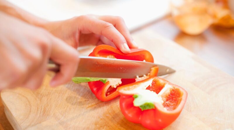 Red pepper on a cutting board with hands and a paring knife